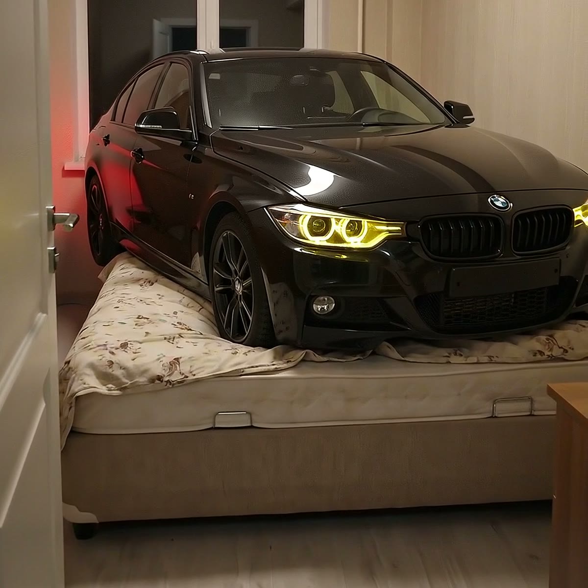 Yatak odasında, yatağın üzerinde duran siyah BMW; farları yanıyor